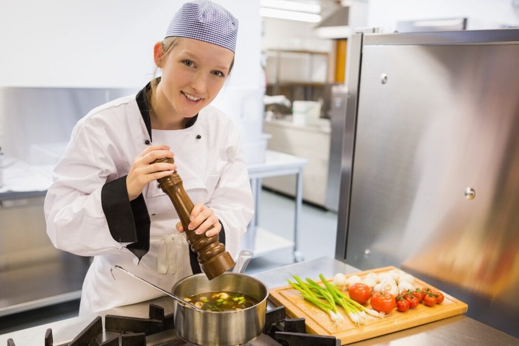 smiling chef adds pepper to cooking vegetables 2026 04 14 00 29 04 utc